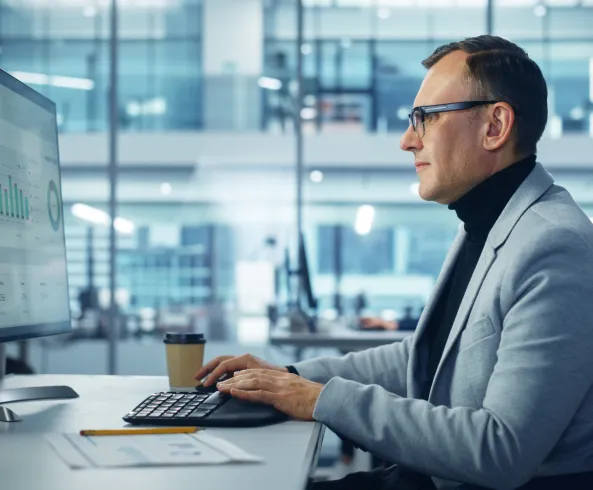 Un hombre de traje casual analizando datos en una computadora de escritorio
