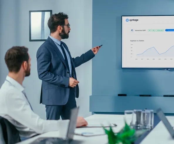 Una persona de traje presentando datos en una pantalla a otra en una sala de juntas